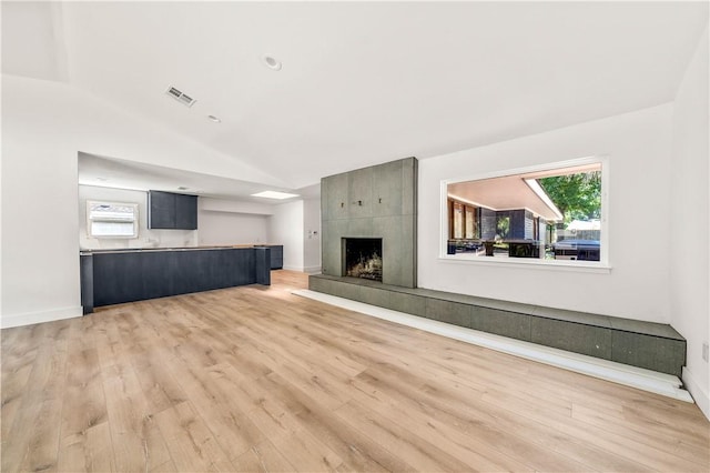 unfurnished living room featuring vaulted ceiling, light hardwood / wood-style flooring, and a tiled fireplace