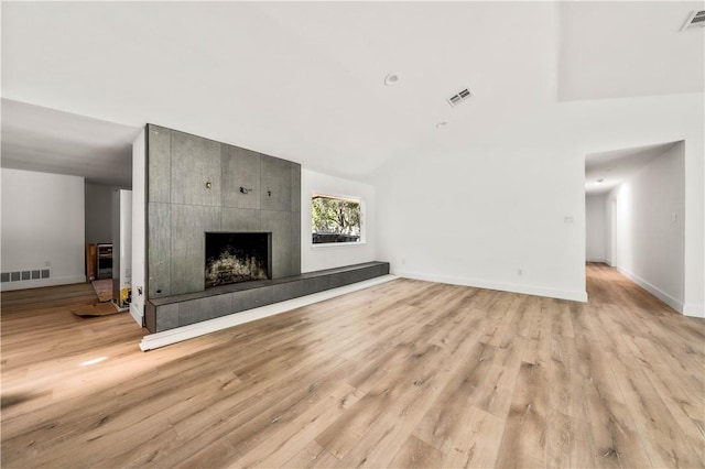 unfurnished living room with a tile fireplace, light wood-type flooring, and vaulted ceiling