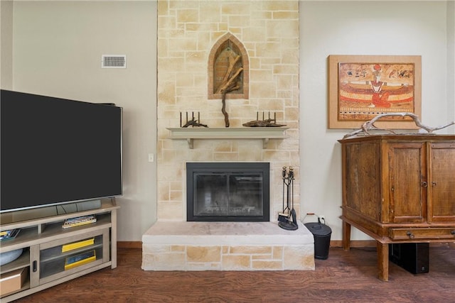 living room with a stone fireplace and dark wood-type flooring