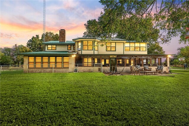 back house at dusk featuring a yard and a patio area