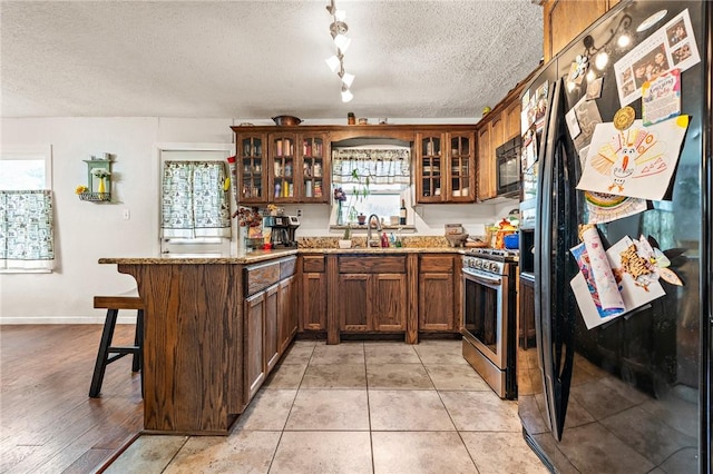 kitchen with light stone countertops, kitchen peninsula, a textured ceiling, black appliances, and light hardwood / wood-style flooring