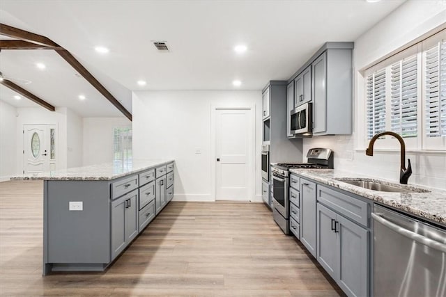 kitchen featuring light stone countertops, appliances with stainless steel finishes, gray cabinetry, and sink