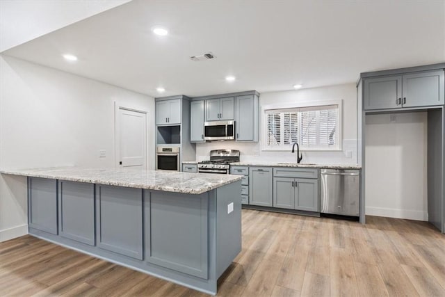 kitchen with light wood-type flooring, light stone countertops, sink, and stainless steel appliances