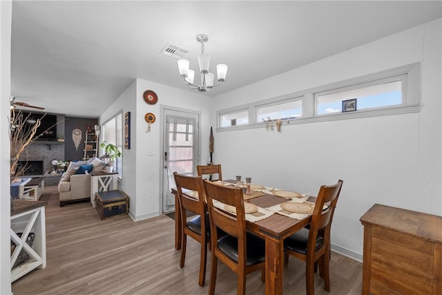 dining area with visible vents, baseboards, an inviting chandelier, a brick fireplace, and light wood-type flooring