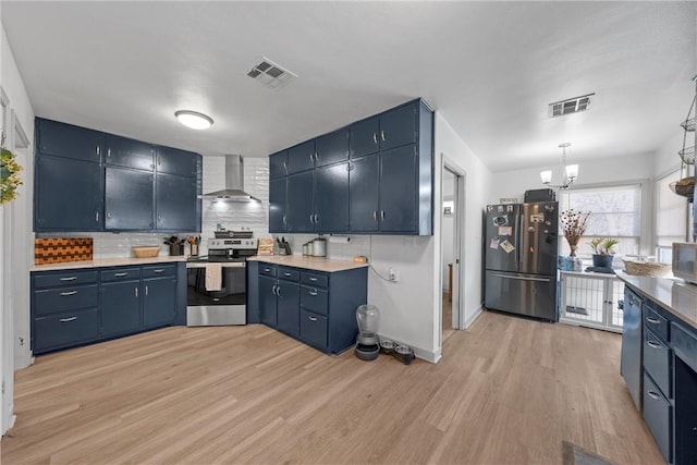 kitchen featuring visible vents, light wood-style floors, appliances with stainless steel finishes, wall chimney range hood, and blue cabinets