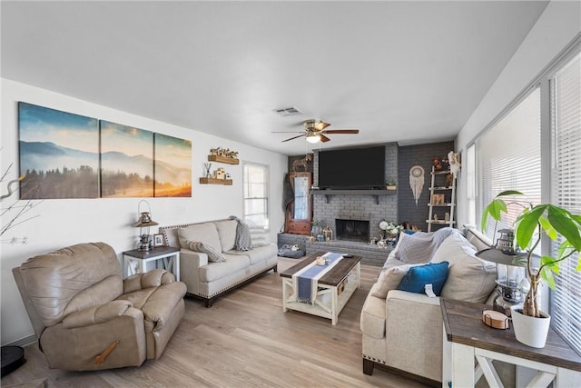 living area with visible vents, a brick fireplace, light wood-type flooring, and a ceiling fan