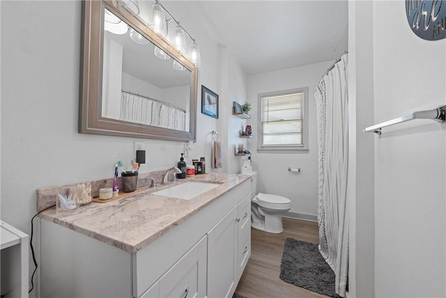 bathroom with toilet, vanity, baseboards, and wood finished floors