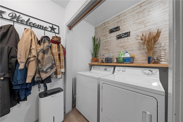 clothes washing area with laundry area, light wood-style flooring, wooden walls, and separate washer and dryer