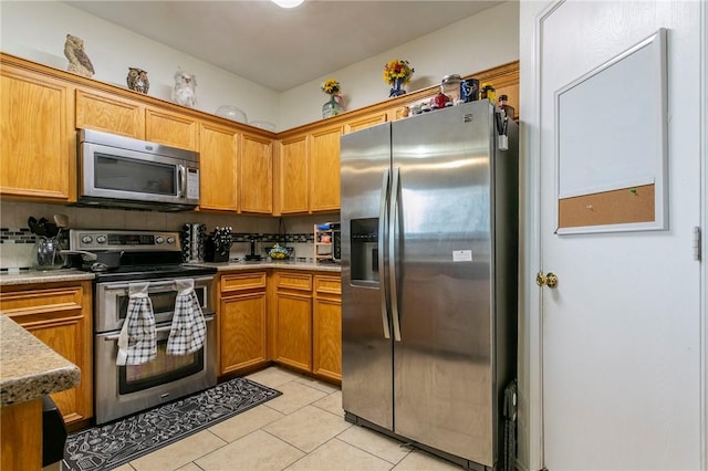 kitchen with light countertops, light tile patterned floors, decorative backsplash, brown cabinets, and stainless steel appliances