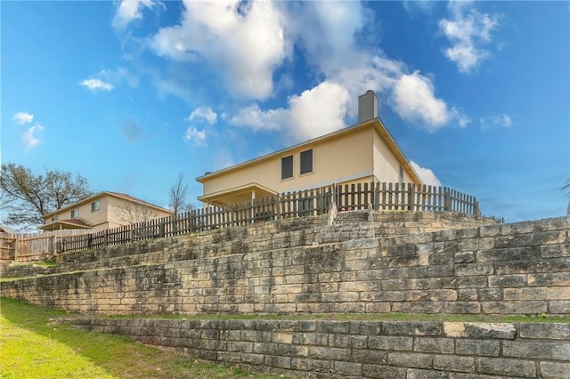 view of side of home with stucco siding, a chimney, and fence