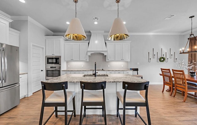 kitchen featuring stainless steel appliances, custom exhaust hood, a center island with sink, and pendant lighting