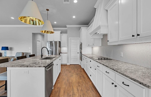 kitchen featuring a breakfast bar area, appliances with stainless steel finishes, an island with sink, decorative light fixtures, and custom exhaust hood