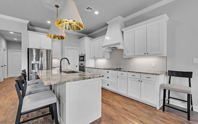 kitchen with sink, premium range hood, a kitchen island with sink, stainless steel appliances, and white cabinets