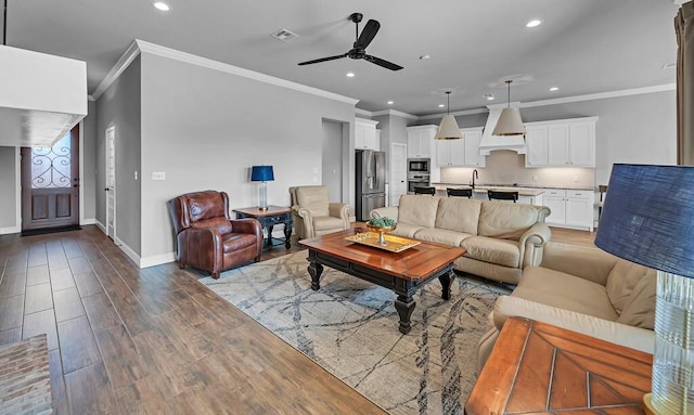 living room featuring sink, wood-type flooring, ornamental molding, and ceiling fan