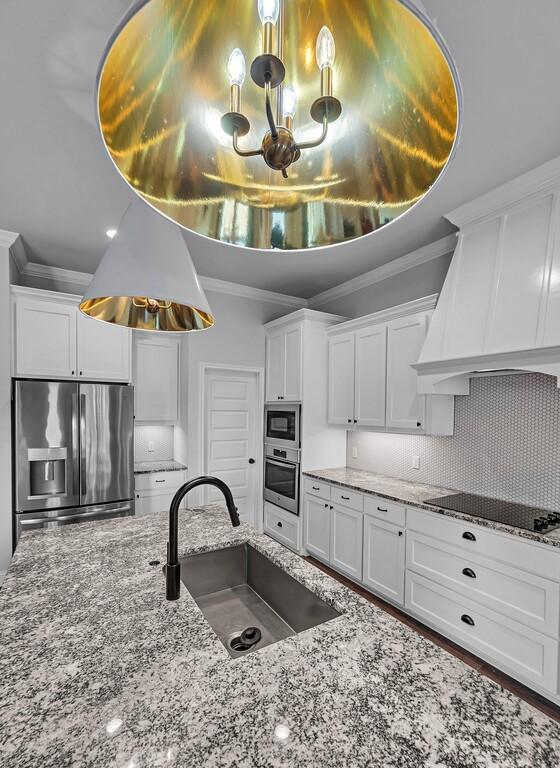 kitchen featuring premium range hood, appliances with stainless steel finishes, sink, white cabinets, and light stone counters