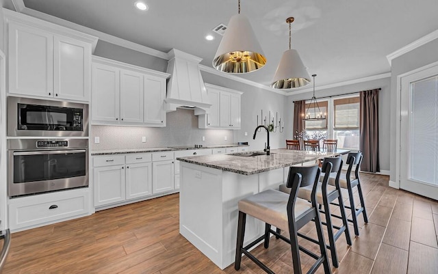 kitchen with sink, white cabinetry, light stone countertops, a kitchen island with sink, and black appliances