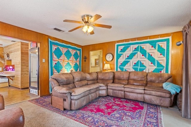 carpeted living area featuring visible vents, wooden walls, ceiling fan, and a textured ceiling