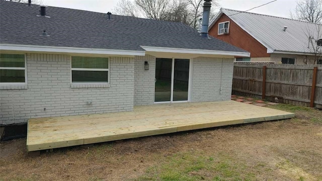 rear view of house featuring a shingled roof, fence, a deck, and brick siding