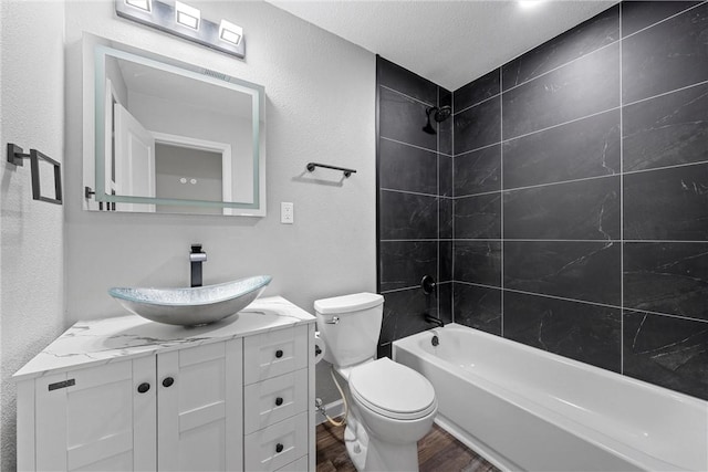 full bath featuring a textured wall, toilet, bathing tub / shower combination, wood finished floors, and vanity