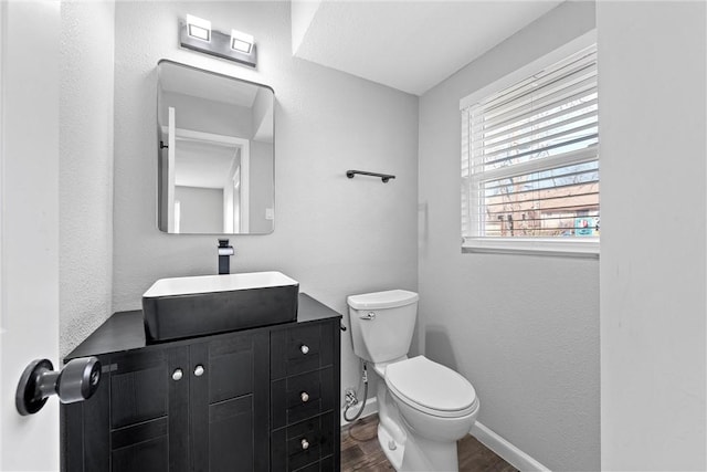 half bathroom featuring baseboards, vanity, toilet, and wood finished floors