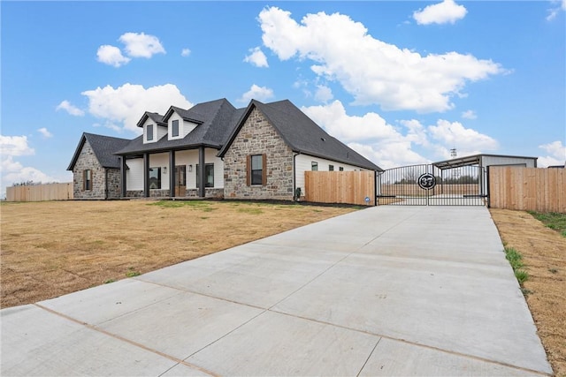 view of front facade with driveway, stone siding, a gate, fence, and a front yard