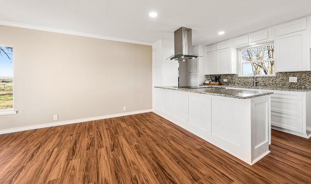 kitchen with white cabinets, wall chimney exhaust hood, light stone counters, and kitchen peninsula