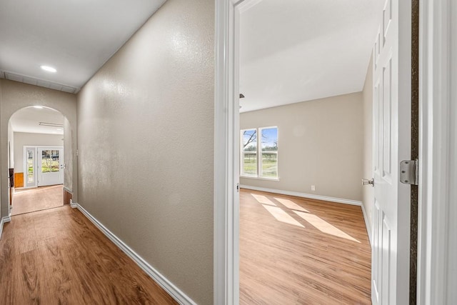 hallway with arched walkways, a textured wall, light wood-style flooring, and baseboards