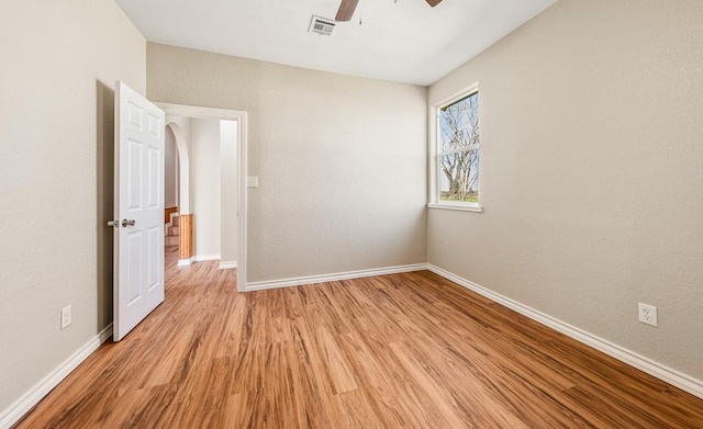 spare room featuring arched walkways, light wood-style flooring, visible vents, and baseboards