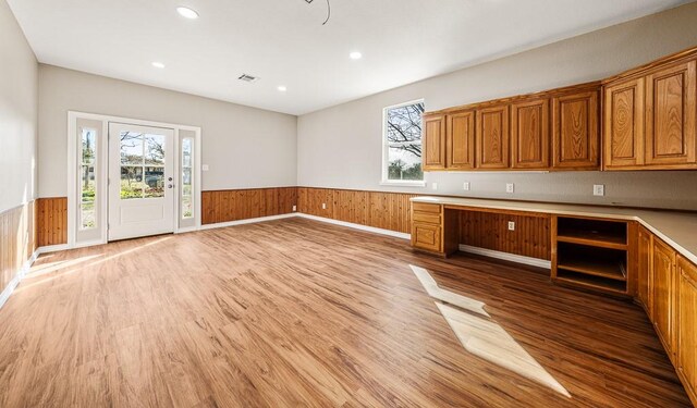 kitchen featuring brown cabinets, a wainscoted wall, light countertops, and built in desk