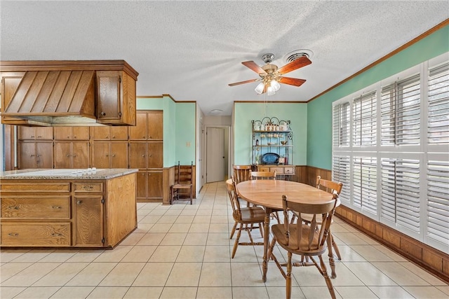 tiled dining room with a textured ceiling, ornamental molding, ceiling fan, and wood walls