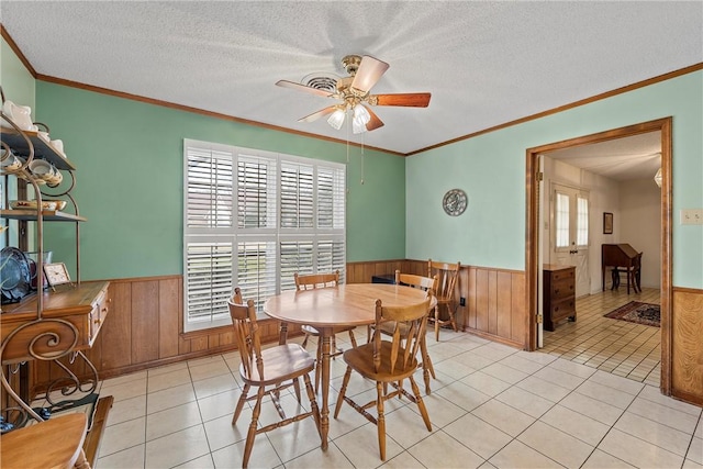 tiled dining area featuring crown molding, ceiling fan, a textured ceiling, and wood walls