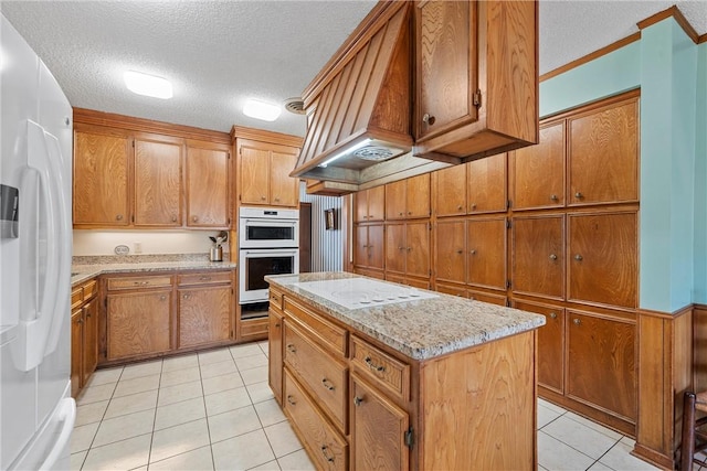 kitchen with light tile patterned flooring, custom exhaust hood, a center island, white appliances, and a textured ceiling