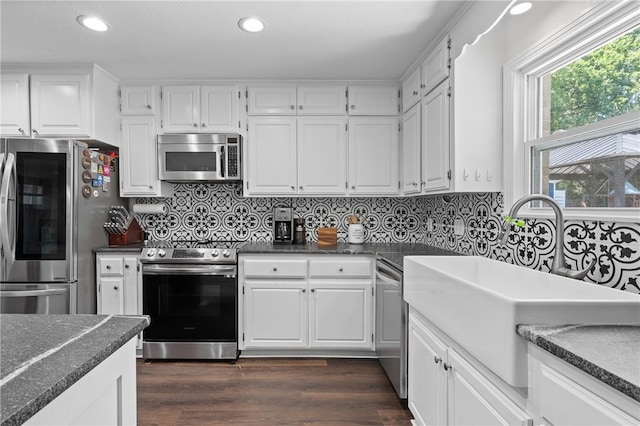 kitchen with appliances with stainless steel finishes, dark wood-type flooring, dark countertops, and a sink