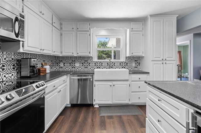 kitchen with white cabinets, dark countertops, dark wood-style flooring, stainless steel appliances, and a sink