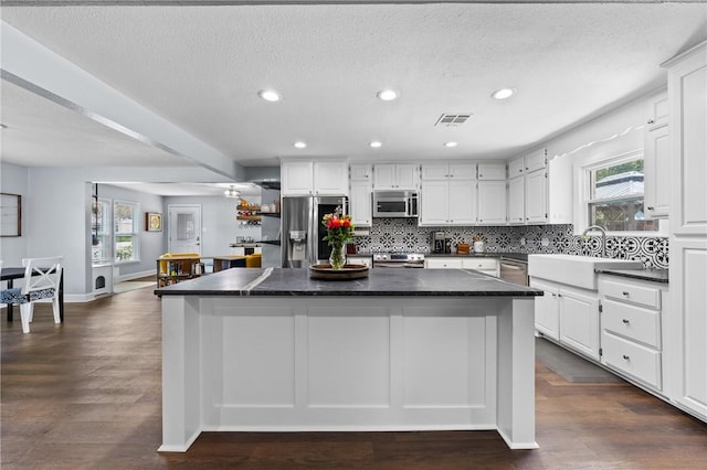 kitchen featuring visible vents, dark countertops, a kitchen island, stainless steel appliances, and a sink