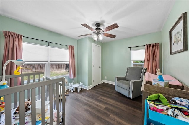 bedroom with a ceiling fan, a nursery area, dark wood finished floors, and baseboards