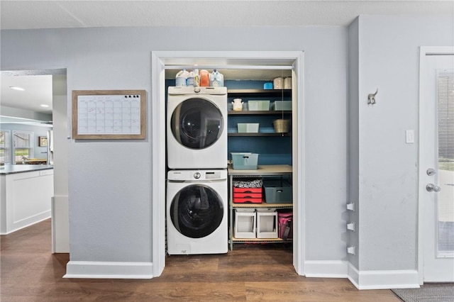 laundry room featuring laundry area, stacked washing maching and dryer, dark wood finished floors, and baseboards