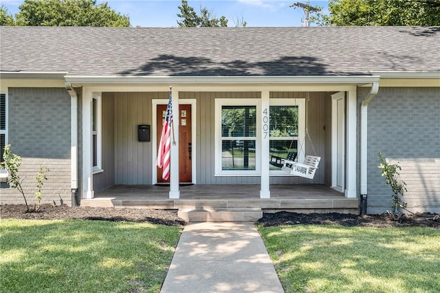 property entrance featuring a shingled roof, covered porch, brick siding, and a lawn