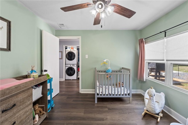 bedroom with a crib, baseboards, visible vents, stacked washer and clothes dryer, and wood finished floors