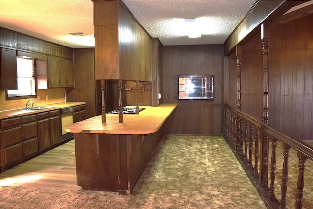 kitchen featuring dishwasher, wood walls, kitchen peninsula, sink, and a textured ceiling