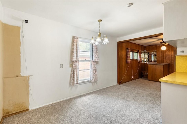 unfurnished room with light carpet, ceiling fan with notable chandelier, and wooden walls