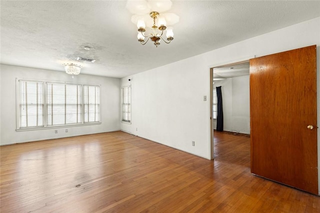 unfurnished room with a chandelier, a textured ceiling, and hardwood / wood-style flooring