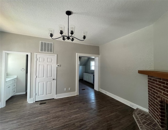 unfurnished dining area featuring a chandelier, a textured ceiling, dark hardwood / wood-style flooring, and a brick fireplace