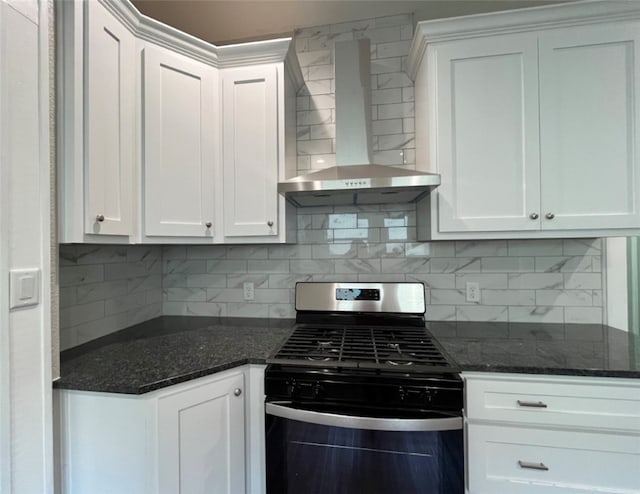 kitchen with tasteful backsplash, dark stone counters, wall chimney exhaust hood, white cabinetry, and stainless steel range with gas stovetop