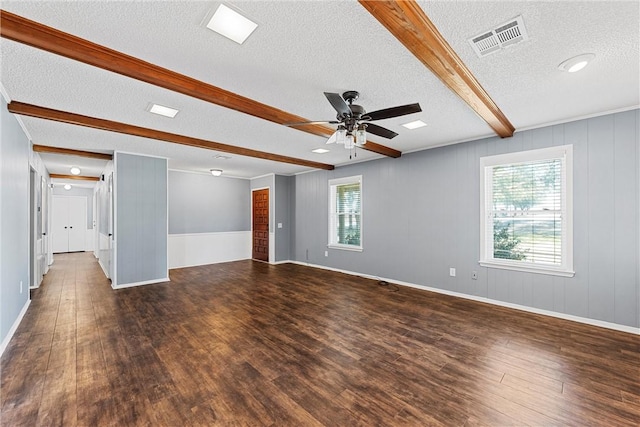 spare room with a textured ceiling, beam ceiling, a wealth of natural light, and dark hardwood / wood-style flooring