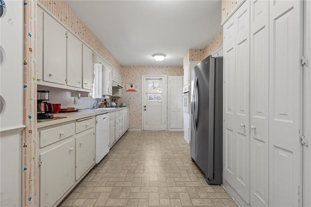 kitchen with brick patterned floor, wallpapered walls, white appliances, white cabinets, and light countertops