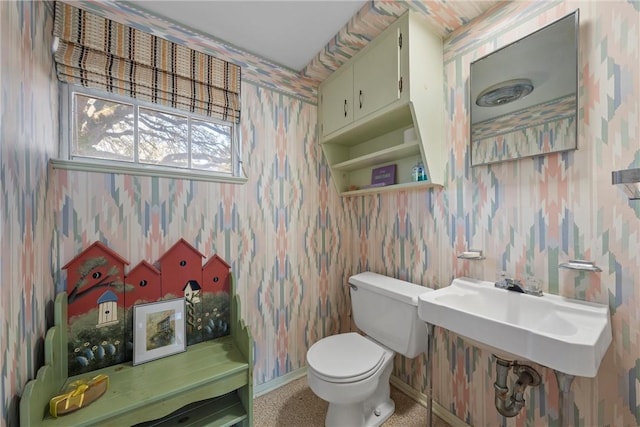 bathroom featuring toilet, wallpapered walls, and baseboards