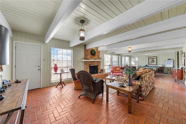 living area featuring beamed ceiling, a fireplace, brick floor, and a wealth of natural light