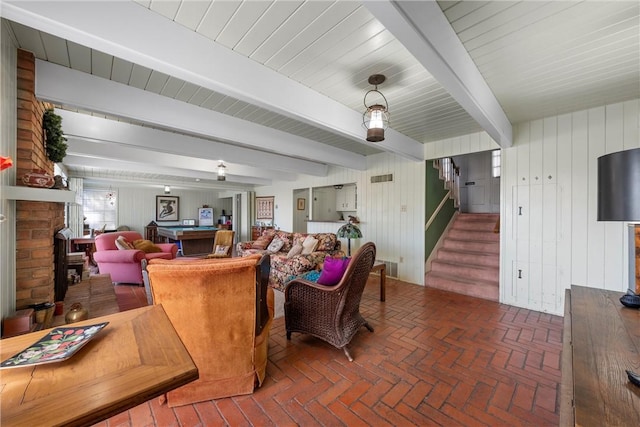 living area with beamed ceiling, visible vents, brick floor, a brick fireplace, and stairs