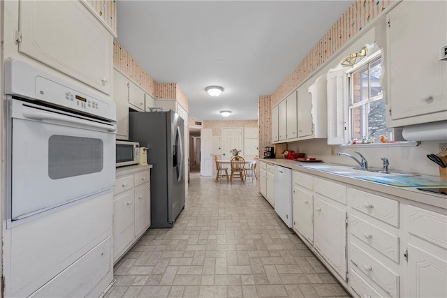 kitchen featuring white appliances, wallpapered walls, a sink, light countertops, and brick patterned floor